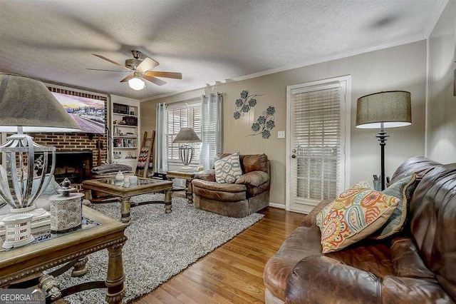 living room featuring a textured ceiling, ornamental molding, ceiling fan, a fireplace, and hardwood / wood-style floors