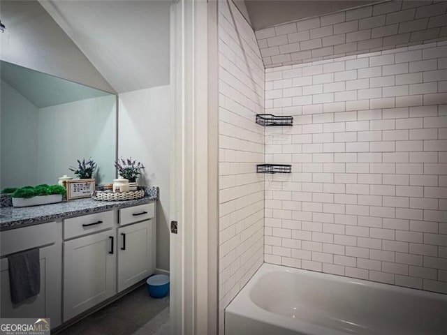 bathroom featuring vanity, tiled shower / bath combo, and vaulted ceiling