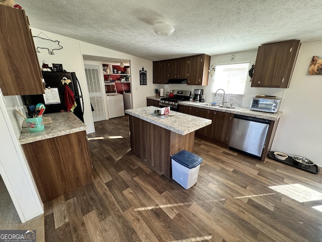 kitchen with sink, dark wood-type flooring, appliances with stainless steel finishes, washing machine and dryer, and a kitchen island