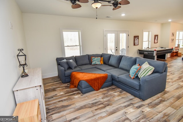 living room with a wealth of natural light, light hardwood / wood-style floors, french doors, and ceiling fan