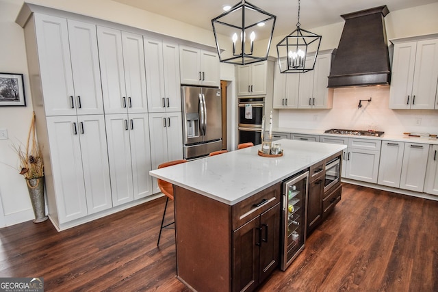 kitchen with appliances with stainless steel finishes, a breakfast bar, beverage cooler, custom exhaust hood, and hanging light fixtures