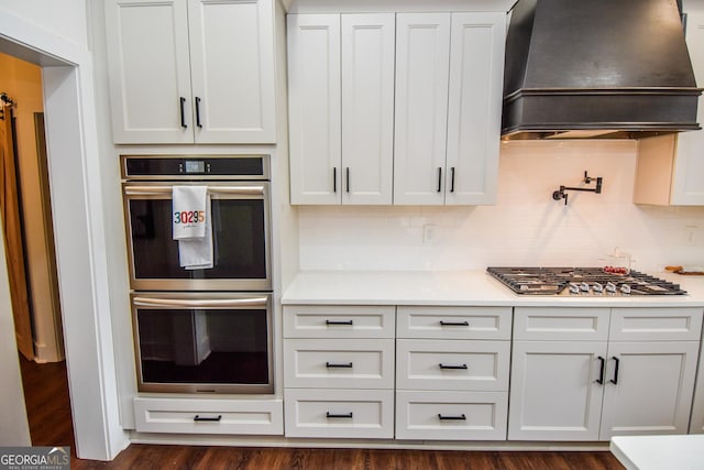 kitchen featuring backsplash, stainless steel appliances, custom range hood, and white cabinets