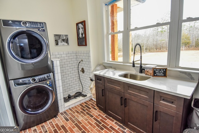 washroom with sink, plenty of natural light, cabinets, and stacked washer and clothes dryer