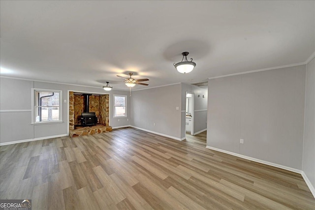 unfurnished living room featuring ornamental molding, a wood stove, ceiling fan, and light wood-type flooring