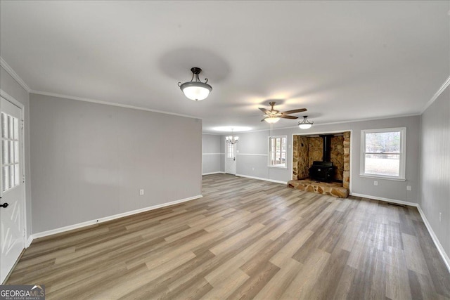 unfurnished living room featuring ornamental molding, a wood stove, ceiling fan with notable chandelier, and light hardwood / wood-style floors