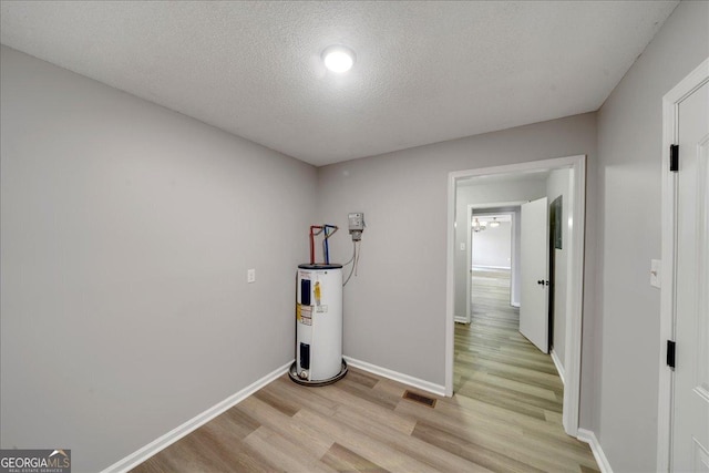 corridor with water heater, a textured ceiling, and light hardwood / wood-style flooring