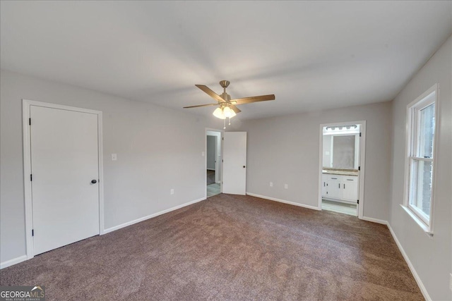 unfurnished bedroom with multiple windows, ensuite bathroom, carpet flooring, and ceiling fan