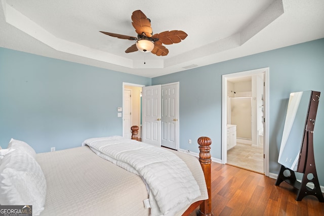 bedroom with hardwood / wood-style flooring, ensuite bath, a raised ceiling, and ceiling fan