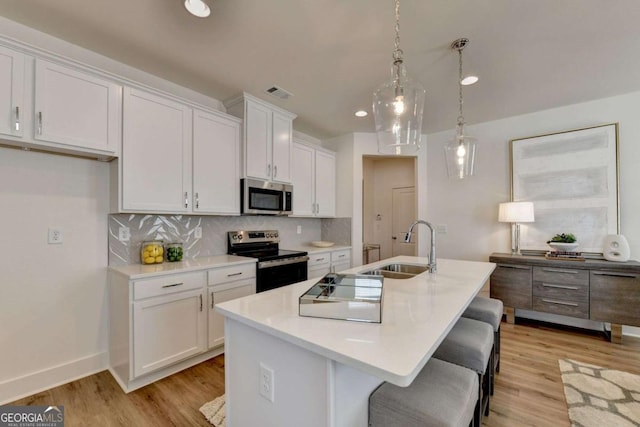 kitchen with sink, white cabinetry, hanging light fixtures, appliances with stainless steel finishes, and a kitchen island with sink