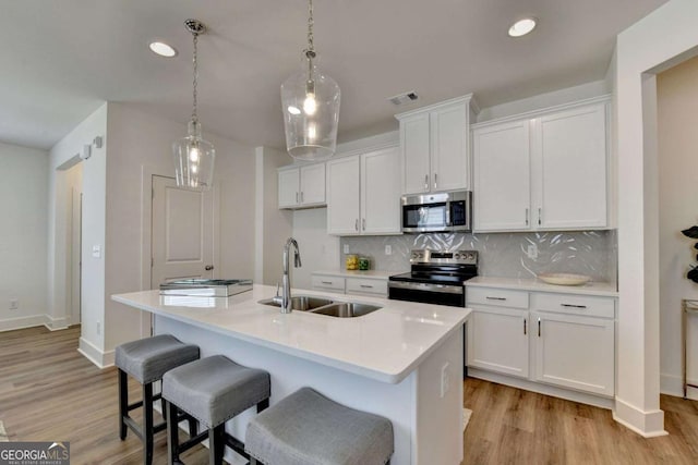 kitchen with white cabinetry, sink, stainless steel appliances, and an island with sink