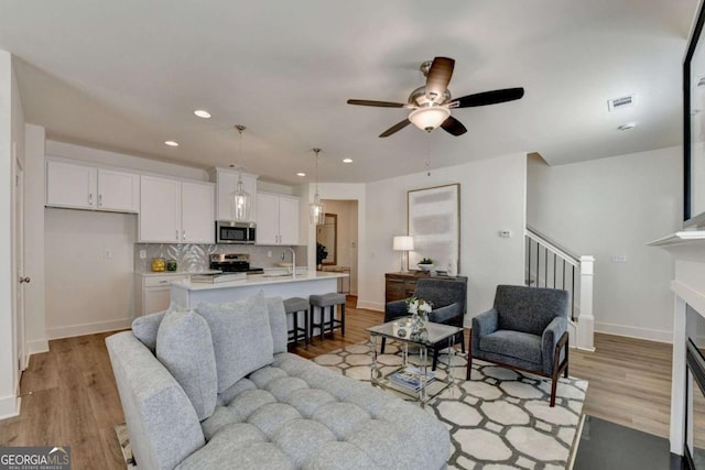 living room featuring ceiling fan, sink, and light hardwood / wood-style floors