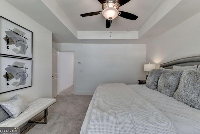 bedroom with a tray ceiling, light colored carpet, and ceiling fan