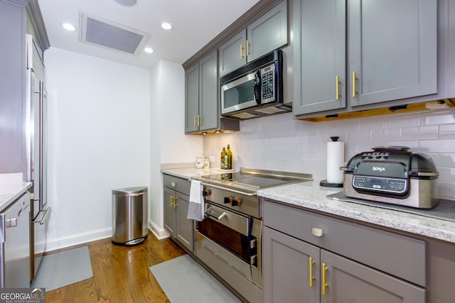 kitchen with visible vents, dark wood-type flooring, light stone counters, stainless steel microwave, and backsplash