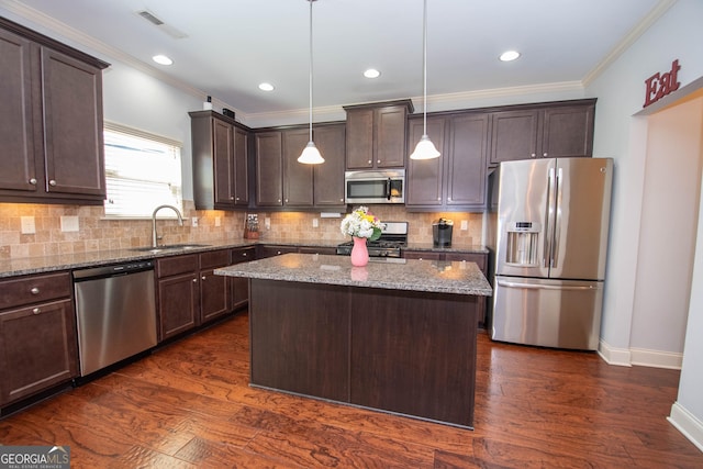 kitchen featuring light stone counters, hanging light fixtures, appliances with stainless steel finishes, a sink, and a kitchen island