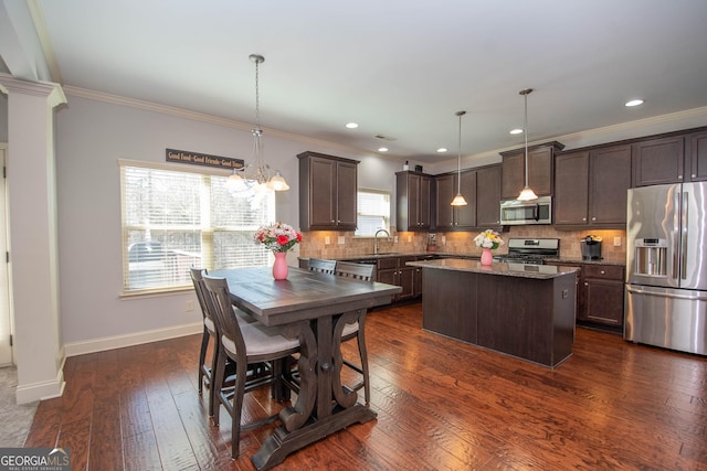 kitchen with a kitchen island, stainless steel appliances, a sink, and decorative light fixtures