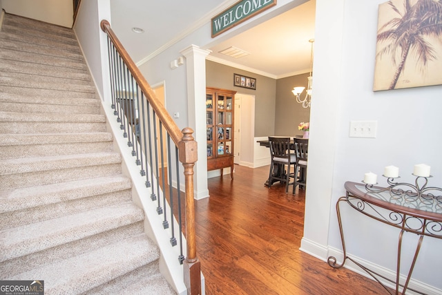 staircase featuring a notable chandelier, wood finished floors, baseboards, decorative columns, and crown molding