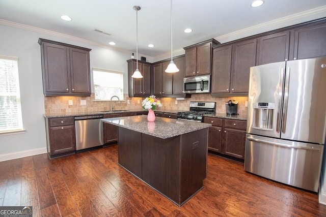 kitchen featuring a kitchen island, dark stone countertops, decorative light fixtures, stainless steel appliances, and a sink