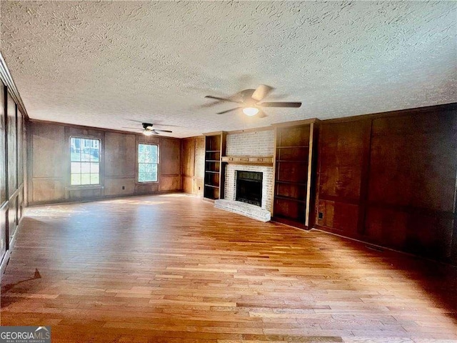 unfurnished living room with built in shelves, a textured ceiling, a fireplace, and light hardwood / wood-style floors