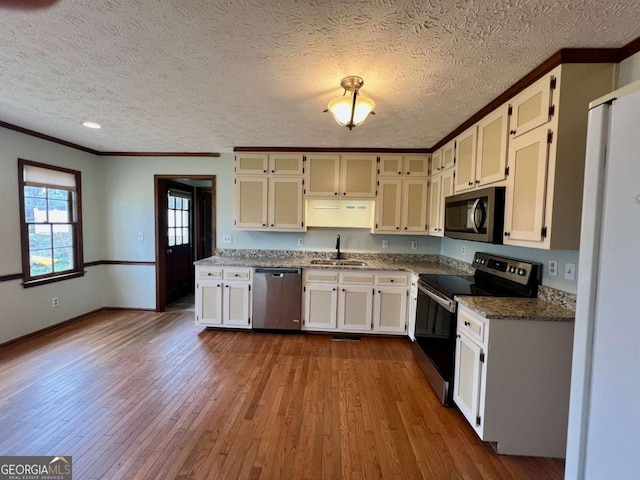 kitchen with sink, hardwood / wood-style flooring, dark stone countertops, stainless steel appliances, and ornamental molding