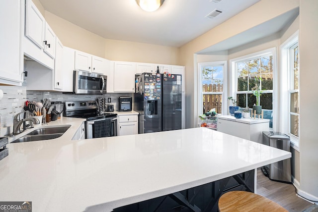 kitchen with sink, appliances with stainless steel finishes, a kitchen breakfast bar, white cabinets, and decorative backsplash