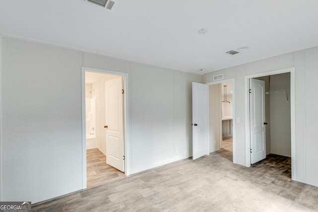 unfurnished bedroom with a walk in closet, visible vents, and wood finished floors