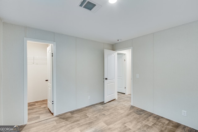 unfurnished bedroom with a closet, light wood-type flooring, a walk in closet, and visible vents