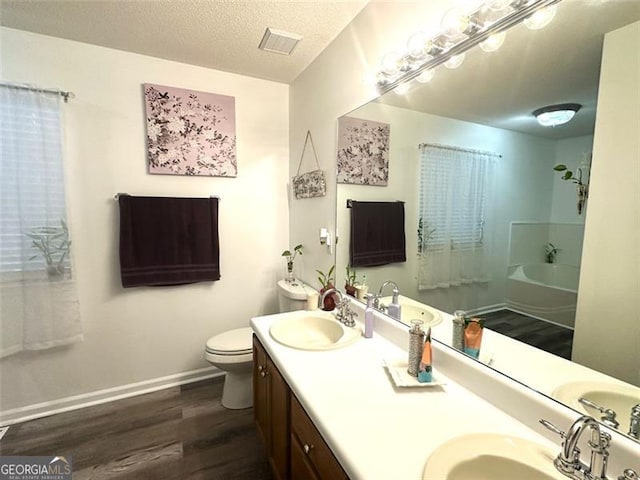 bathroom featuring hardwood / wood-style floors, vanity, a textured ceiling, a tub to relax in, and toilet