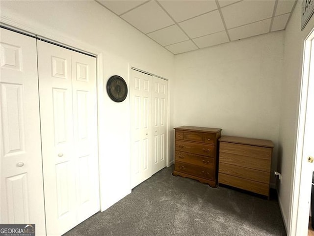 unfurnished bedroom with two closets, a paneled ceiling, and dark colored carpet