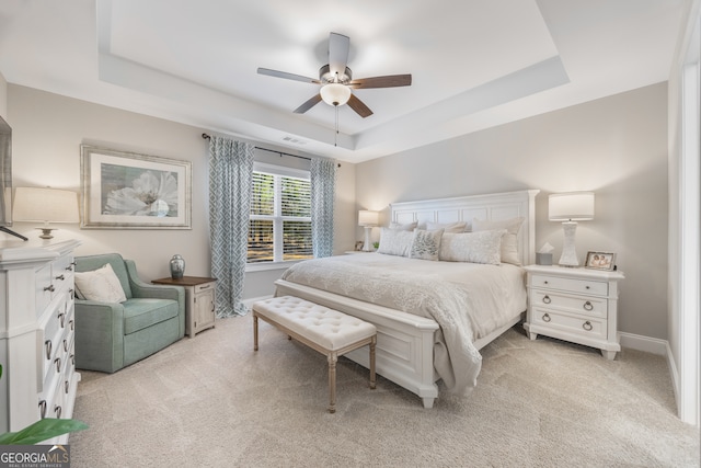 bedroom featuring a raised ceiling, light carpet, ceiling fan, and baseboards