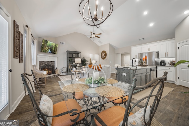 dining room featuring a stone fireplace, dark wood-style flooring, visible vents, baseboards, and vaulted ceiling