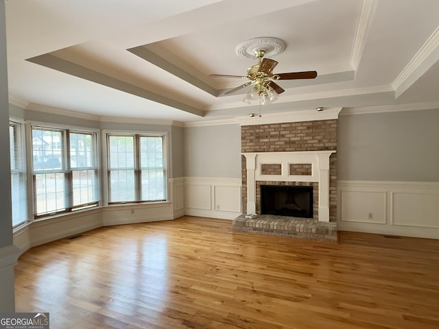 unfurnished living room with a tray ceiling, a fireplace, light hardwood / wood-style floors, and ceiling fan