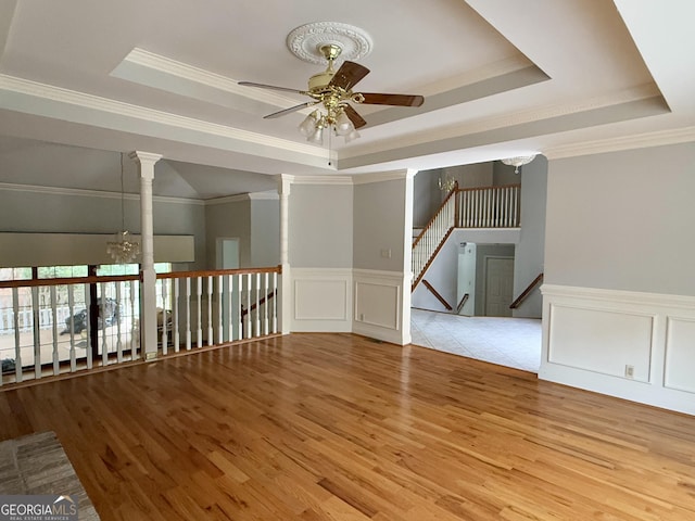 spare room featuring crown molding, a raised ceiling, ceiling fan with notable chandelier, and light wood-type flooring