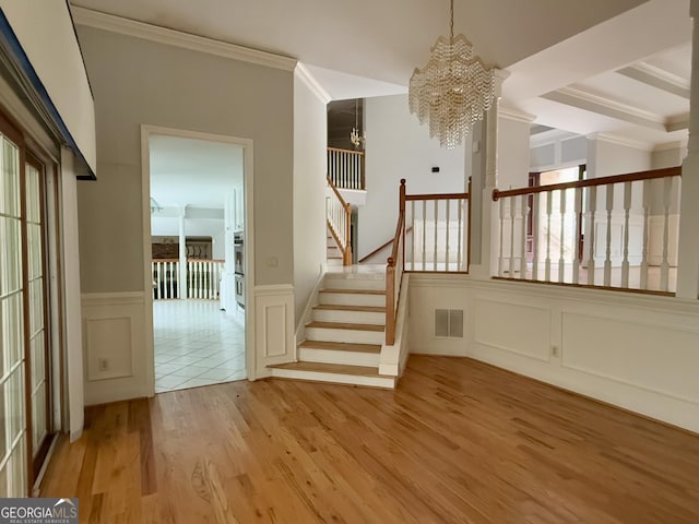 stairs featuring crown molding, a healthy amount of sunlight, hardwood / wood-style floors, and an inviting chandelier