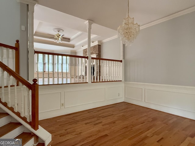 stairs featuring ceiling fan with notable chandelier, decorative columns, hardwood / wood-style flooring, a raised ceiling, and crown molding