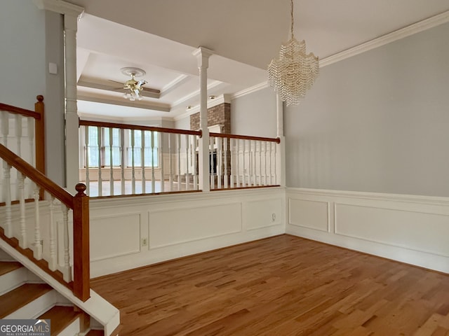 staircase featuring crown molding, ceiling fan with notable chandelier, wood-type flooring, and a raised ceiling