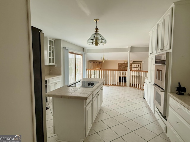 kitchen with tile countertops, black electric stovetop, white cabinets, and decorative light fixtures