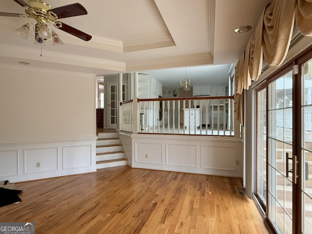 spare room featuring a raised ceiling, ornamental molding, ceiling fan with notable chandelier, and light hardwood / wood-style floors