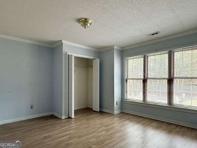 unfurnished bedroom featuring crown molding, a textured ceiling, a closet, and light wood-type flooring