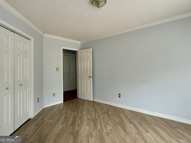 unfurnished bedroom featuring crown molding, a textured ceiling, light wood-type flooring, and a closet