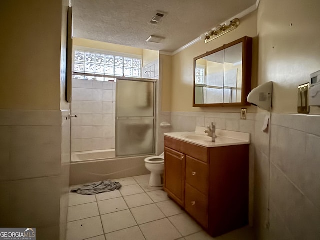 full bathroom with tile patterned floors, toilet, a textured ceiling, tile walls, and enclosed tub / shower combo