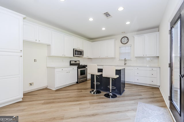 kitchen with a kitchen bar, sink, white cabinetry, a kitchen island, and stainless steel appliances