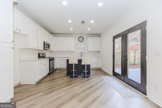 kitchen featuring a kitchen island, white cabinets, backsplash, stainless steel appliances, and french doors