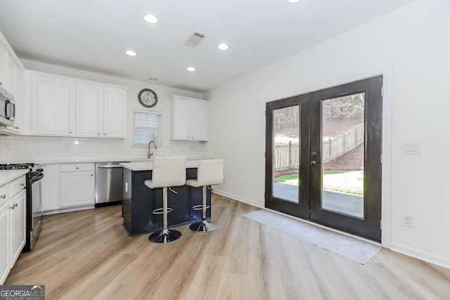 kitchen with french doors, tasteful backsplash, a kitchen island, stainless steel appliances, and white cabinets