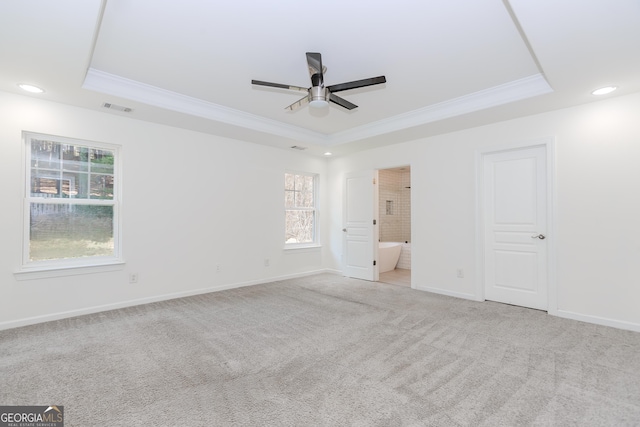 unfurnished bedroom featuring a tray ceiling, ornamental molding, light colored carpet, and ensuite bath