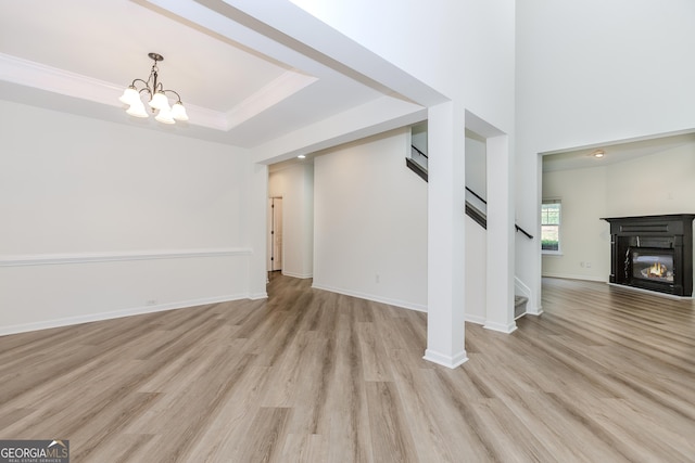 unfurnished living room featuring ornamental molding, a tray ceiling, light hardwood / wood-style floors, and a notable chandelier