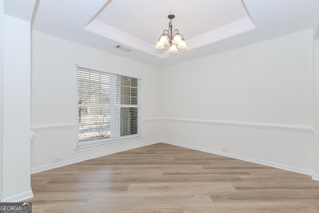 unfurnished room with crown molding, a notable chandelier, a tray ceiling, and light wood-type flooring