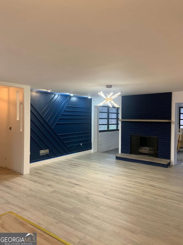 unfurnished living room with light wood-type flooring, a notable chandelier, and a fireplace