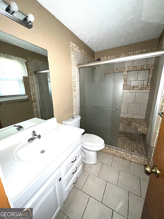 bathroom with tile patterned floors, toilet, a textured ceiling, vanity, and a shower with door