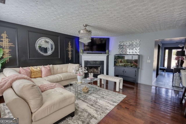 living room featuring an inviting chandelier, a high end fireplace, dark wood-type flooring, and a textured ceiling