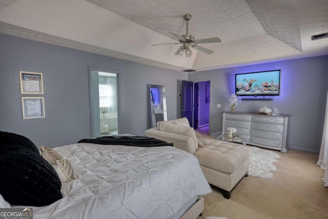 bedroom featuring ensuite bath, ceiling fan, a textured ceiling, light colored carpet, and a raised ceiling